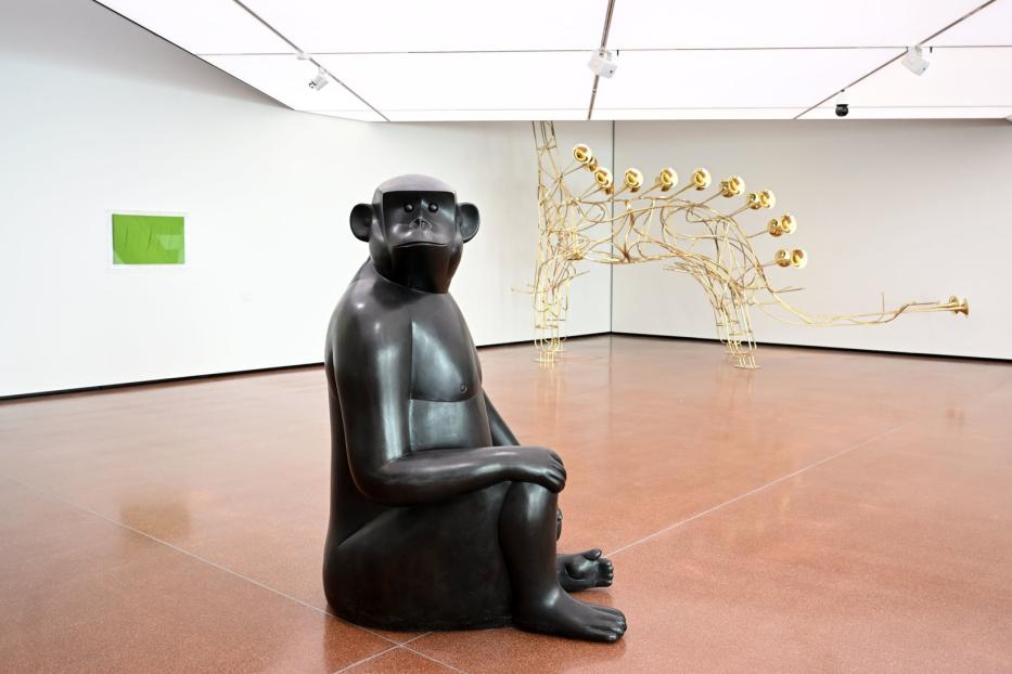 Eine dunkle Affenskulptur sitzt in einer Kunstgalerie.