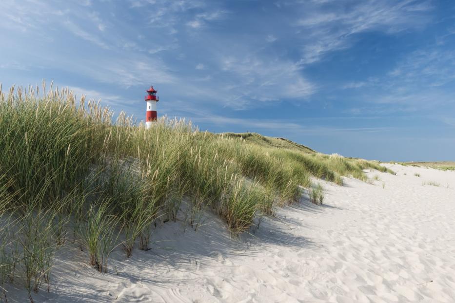 Ein rot-weiß gestreifter Leuchtturm hinter einer Düne mit Strandhafer.