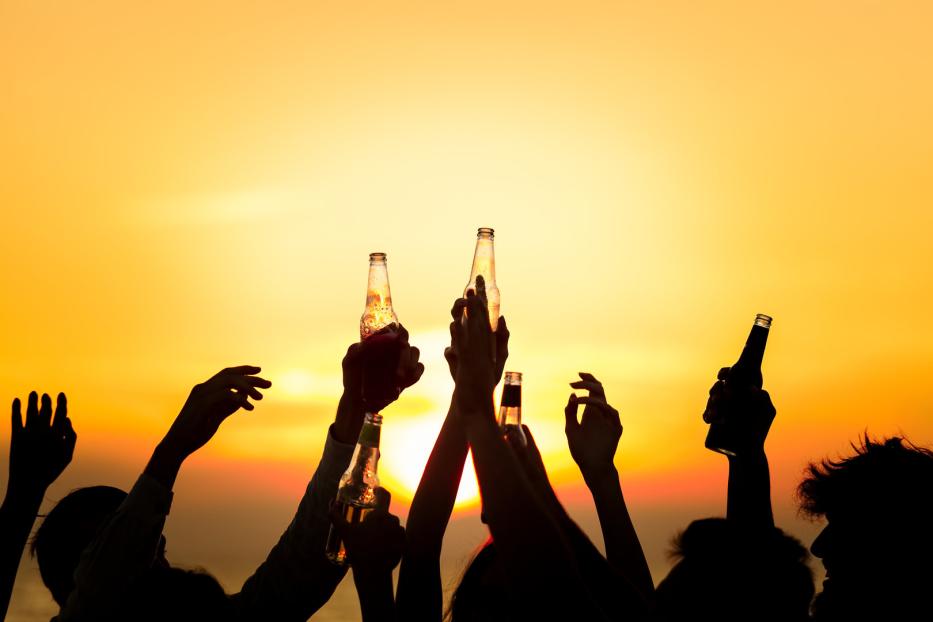 Menschen stoßen bei Sonnenuntergang mit Bierflaschen an.