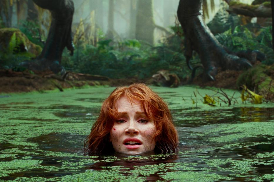 Eine Frau watet durch einen grünen Sumpf, während im Hintergrund Dinosaurierfüße zu sehen sind.