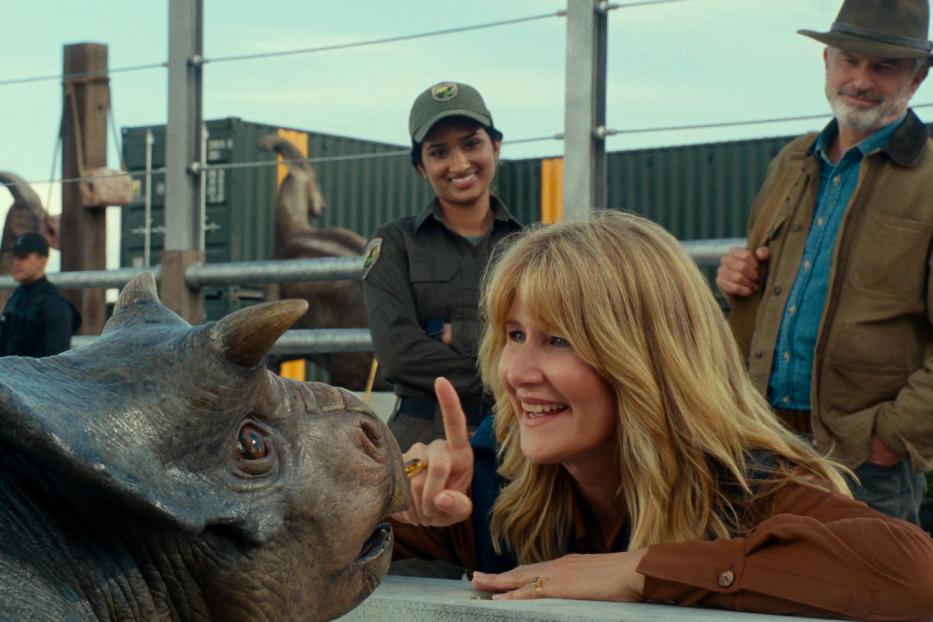 Laura Dern interagiert mit einem Triceratops, während Sam Neill und eine Parkangestellte zusehen.