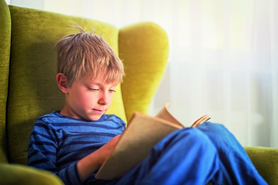 Ein kleiner Junge liest ein Buch in einem grünen Sessel.