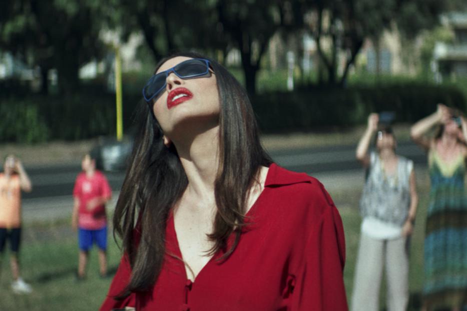 Eine Frau mit Sonnenbrille und roter Bluse blickt in den Himmel.