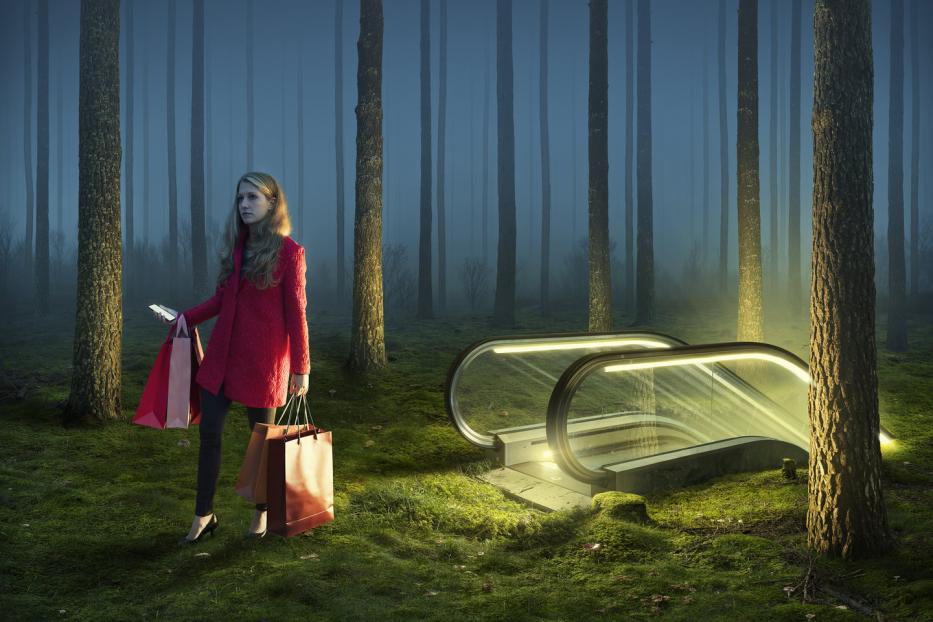 Eine Frau mit Einkaufstüten steht in einem Wald neben einer Rolltreppe.