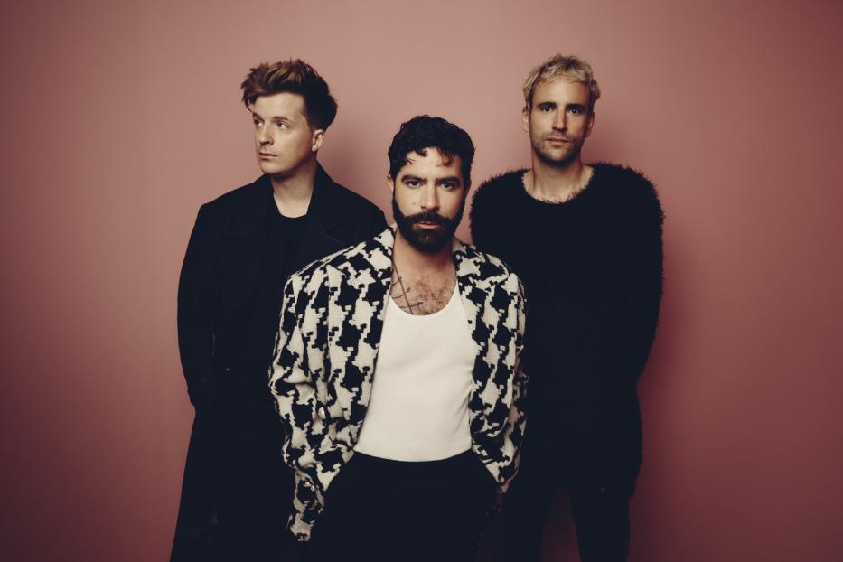 Die Band Foals posiert vor einem rosafarbenen Hintergrund.