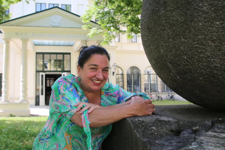 Eine lächelnde Frau lehnt an einer Steinkugel vor dem Max Reinhardt Seminar.