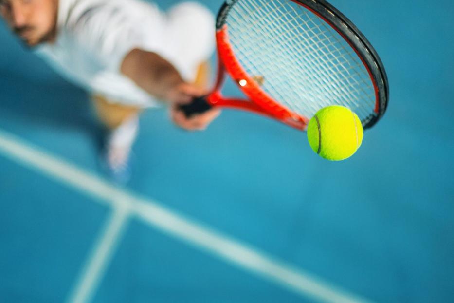 Ein Tennisspieler schlägt einen gelben Ball mit einem roten Schläger.