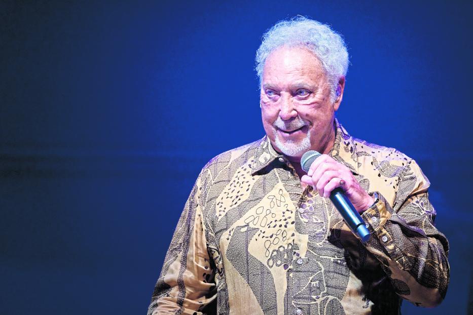 Tom Jones hält ein Mikrofon und lächelt.
