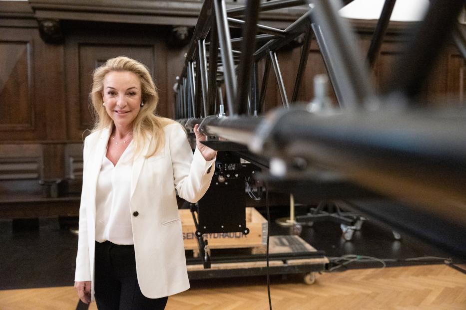 Eine Frau in einem weißen Blazer steht neben einer Bühnenkonstruktion.