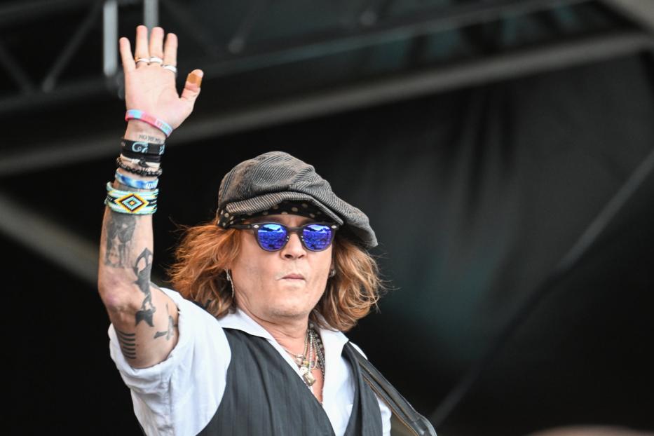 Johnny Depp mit Schirmmütze und Sonnenbrille hebt die Hand.