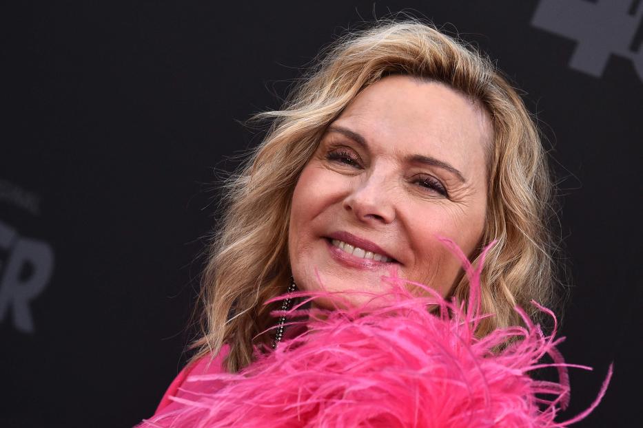 Kim Cattrall lächelt mit einer pinkfarbenen Federboa um den Hals.