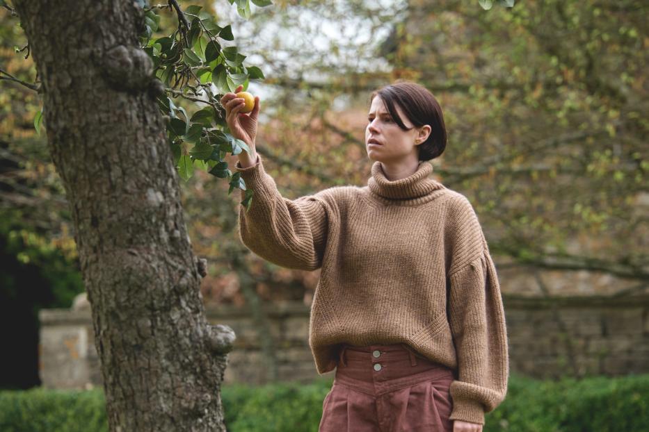 Eine Frau in einem Garten pflückt eine gelbe Frucht von einem Baum.