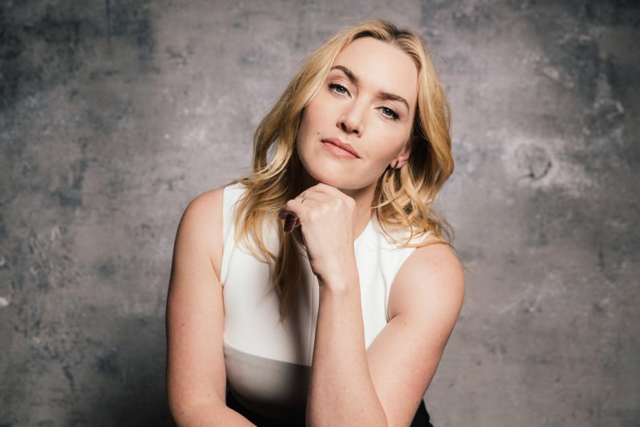 Kate Winslet posiert vor einer grauen Wand.