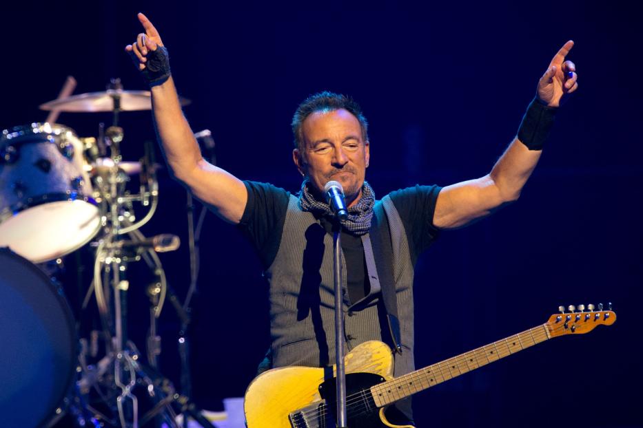 Bruce Springsteen tritt mit erhobenen Armen und Gitarre auf einer Bühne auf.
