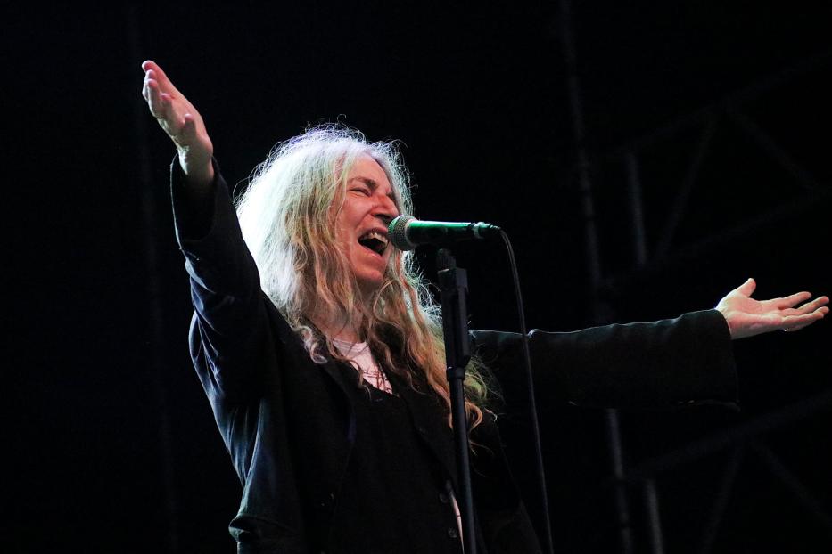 Patti Smith singt mit erhobenen Armen auf der Bühne.
