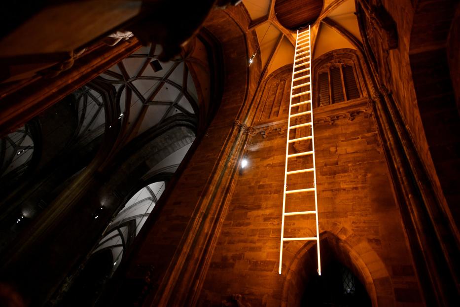 Eine leuchtende Leiter reicht in einer Kirche bis zur Decke.