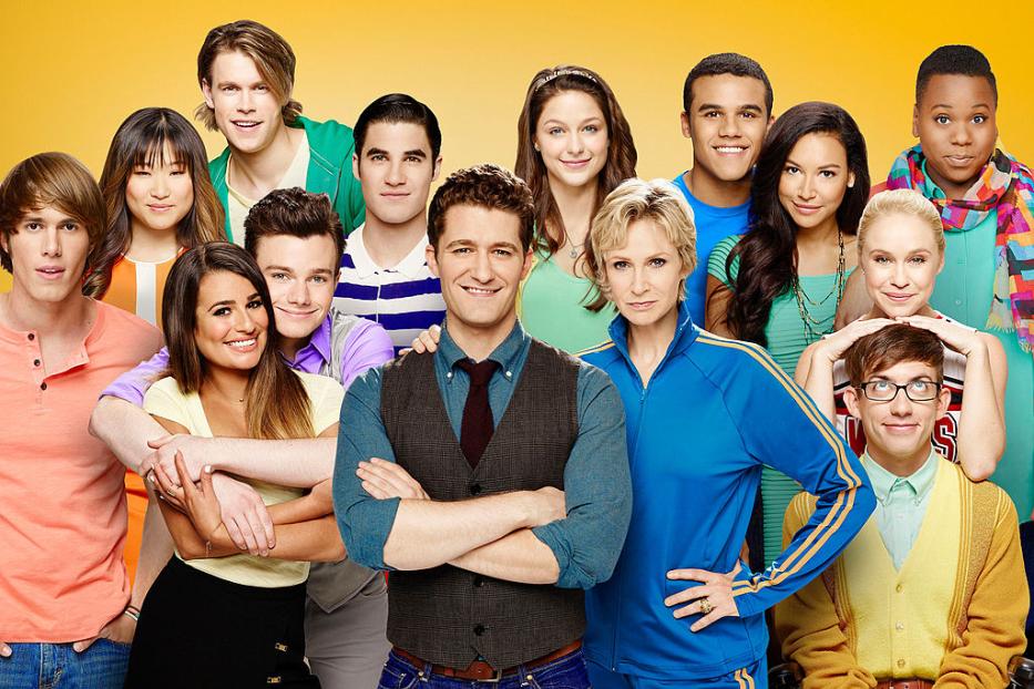 Die Besetzung der Fernsehserie „Glee“ posiert vor einem gelben Hintergrund.