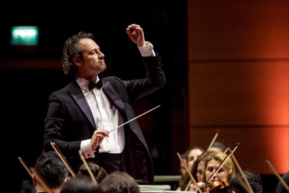 Ein Dirigent leitet ein Orchester mit Geigen.