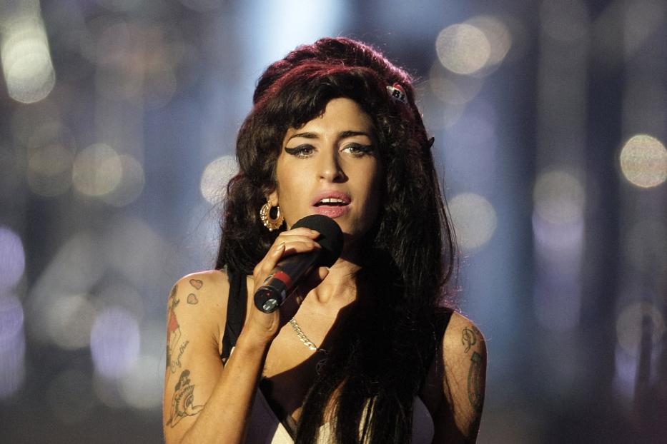 Amy Winehouse singt mit einem Mikrofon in der Hand auf einer Bühne.