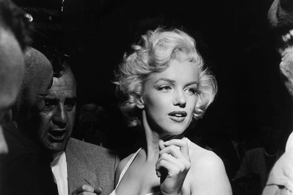 Marilyn Monroe umringt von Menschen bei einer Veranstaltung.