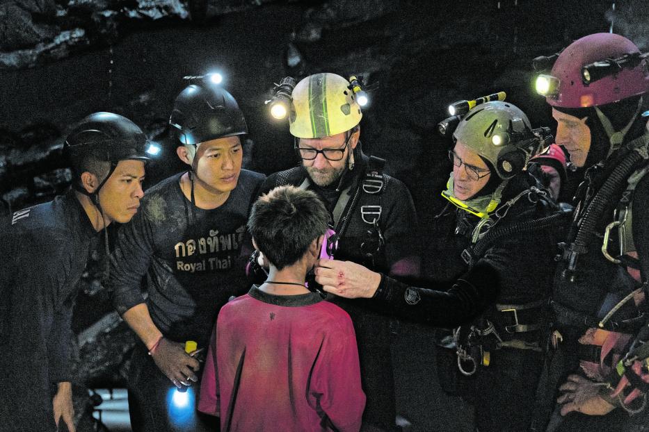 Ein Taucher befestigt Ausrüstung an einem Jungen in einer dunklen Höhle, umgeben von Helfern.