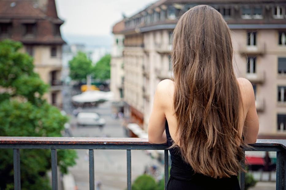 Eine Frau steht auf einem Balkon und blickt auf die Stadt.