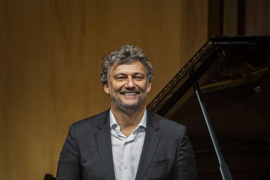 Ein Mann in einem Anzug steht lächelnd vor einem Steinway-Flügel.