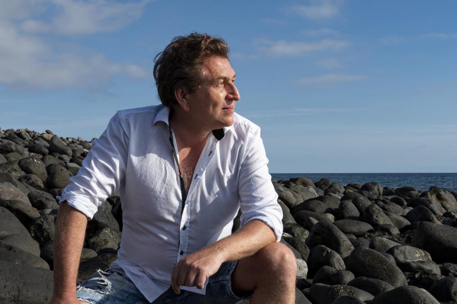 Ein Mann sitzt auf einem Felsenstrand und blickt aufs Meer.