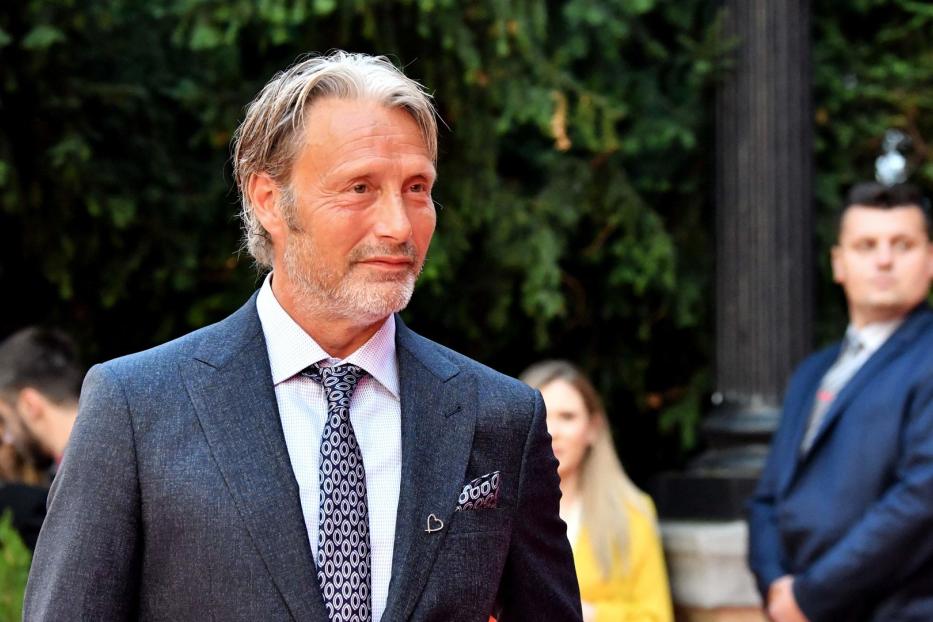 Mads Mikkelsen in einem grauen Anzug mit gemusterter Krawatte.