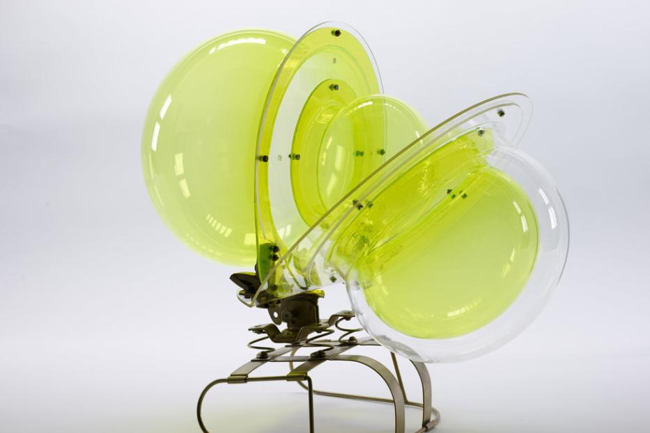 Eine abstrakte Skulptur aus gelbem Glas und Metall auf einem weißen Hintergrund.