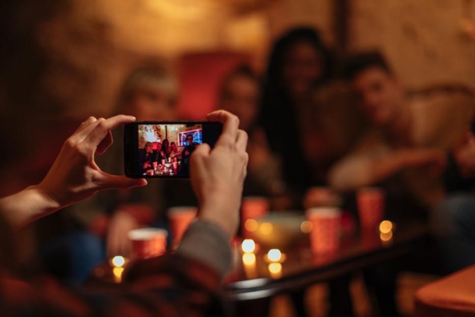 Eine Person fotografiert mit dem Handy eine Gruppe von Freunden auf einer Party.