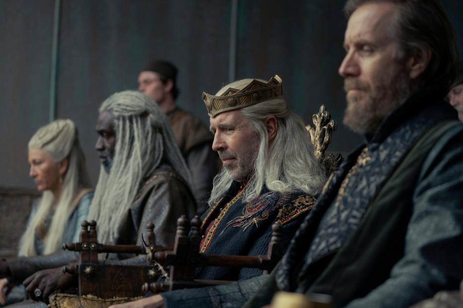 König Viserys Targaryen sitzt mit anderen Würdenträgern auf einem Thron.
