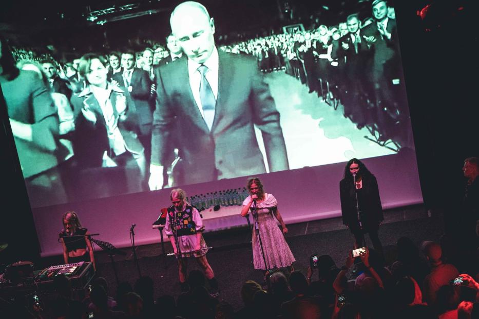Eine Band tritt vor einer Leinwand mit einem Bild von Wladimir Putin auf.