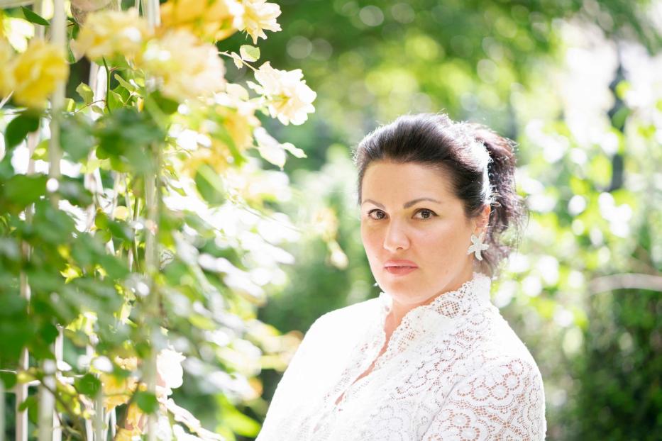 Eine Frau mit weißer Spitze steht vor gelben Rosen.