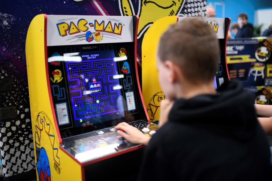 Ein Junge spielt an einem gelben Pac-Man-Spielautomaten.