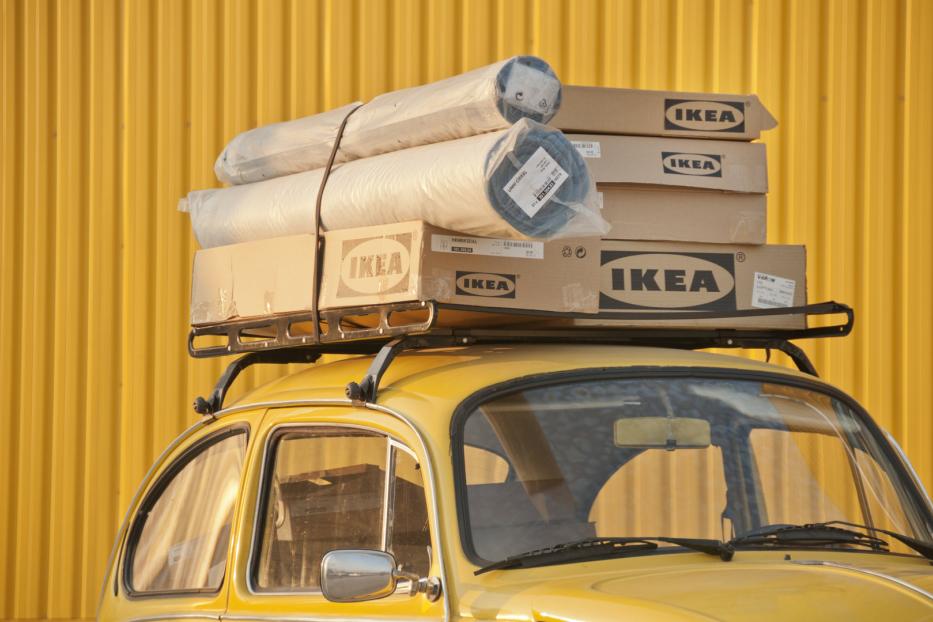 Ein gelber VW Käfer mit IKEA-Paketen und Teppichen auf dem Dachgepäckträger.