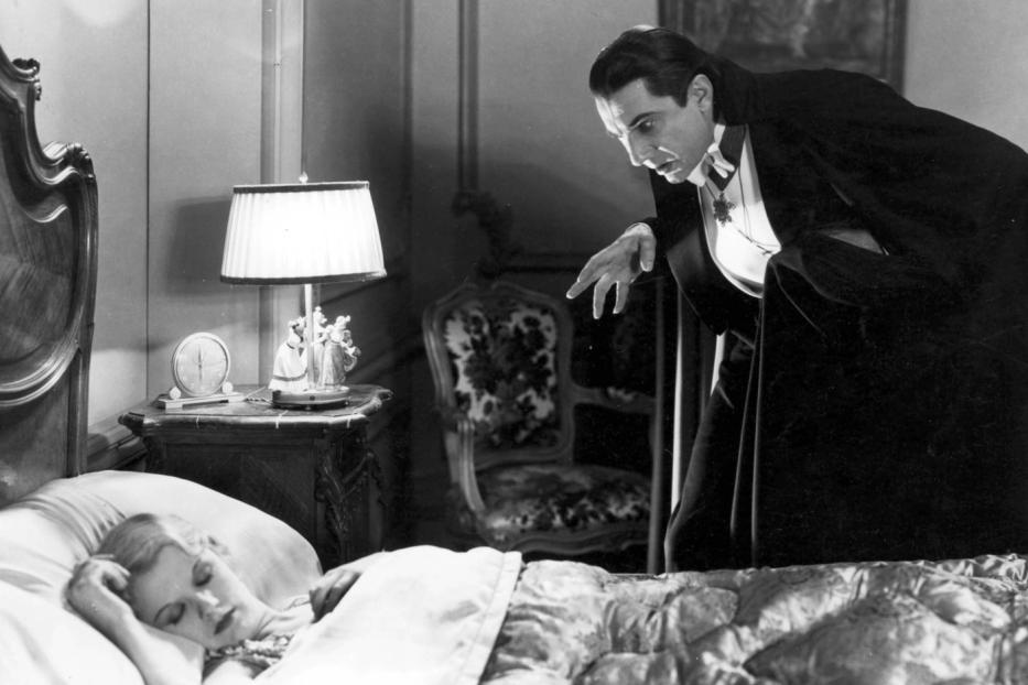 Bela Lugosi als Graf Dracula steht über einer schlafenden Frau im Film „Dracula“ (1931).