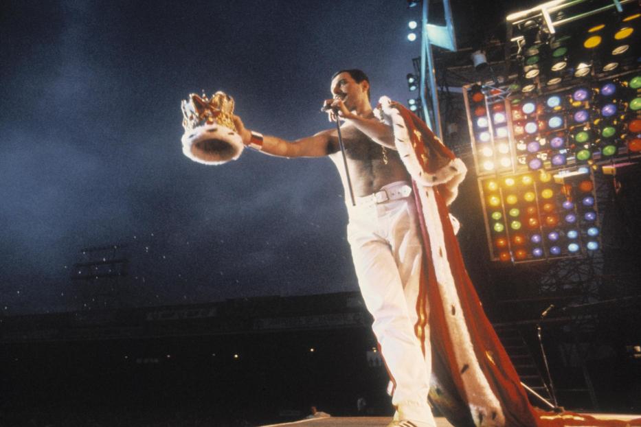 Freddie Mercury mit Krone und Umhang auf der Bühne.