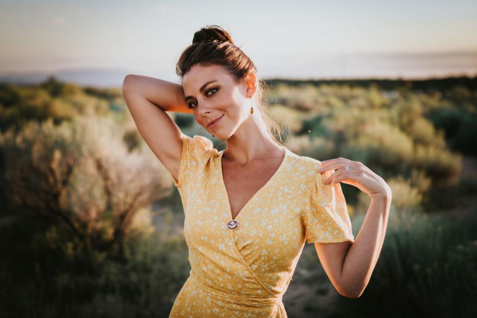 Eine Frau in einem gelben Kleid posiert in einer Landschaft.