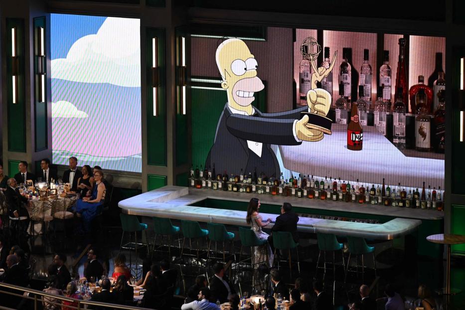 Homer Simpson hält eine Emmy-Trophäe vor einer Bar mit unzähligen Flaschen.