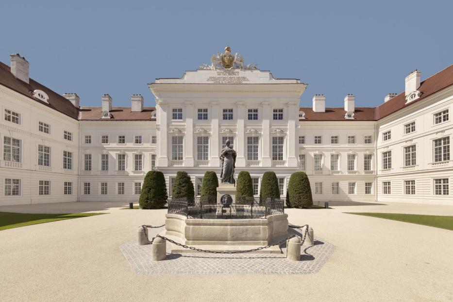 Das Schloss Hof mit einem Brunnen und einer Statue im Vordergrund.