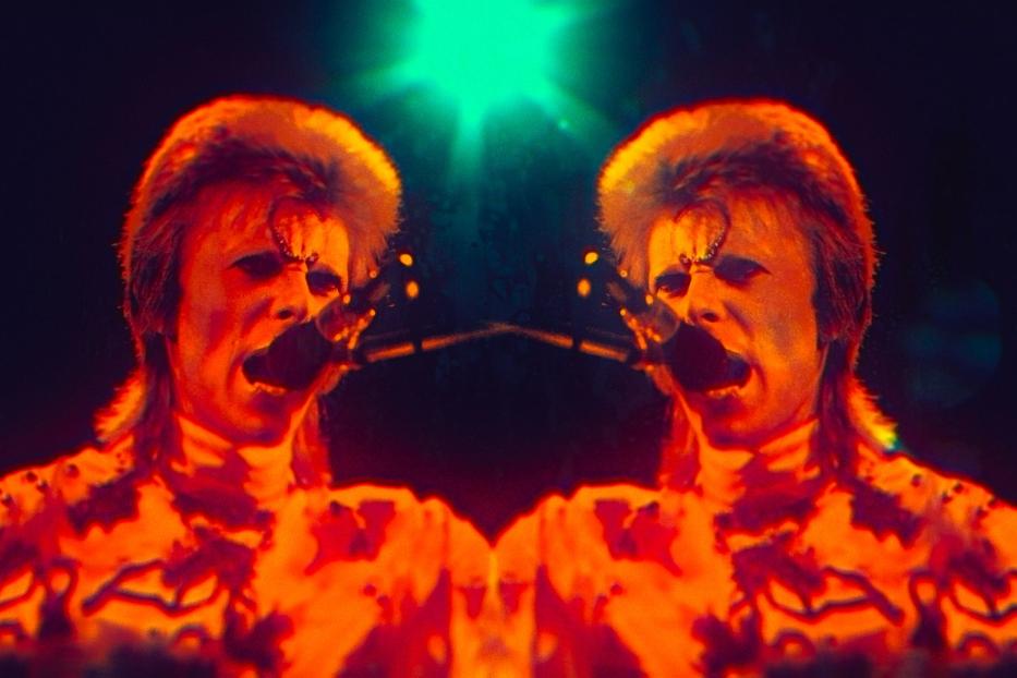 Ein verzerrtes Doppelbild von David Bowie, der in ein Mikrofon singt.