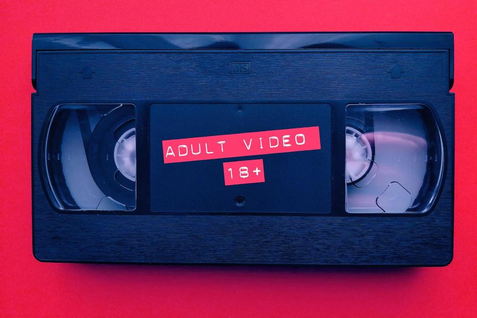 Eine VHS-Kassette mit dem Aufdruck „Adult Video 18+“ vor rotem Hintergrund.