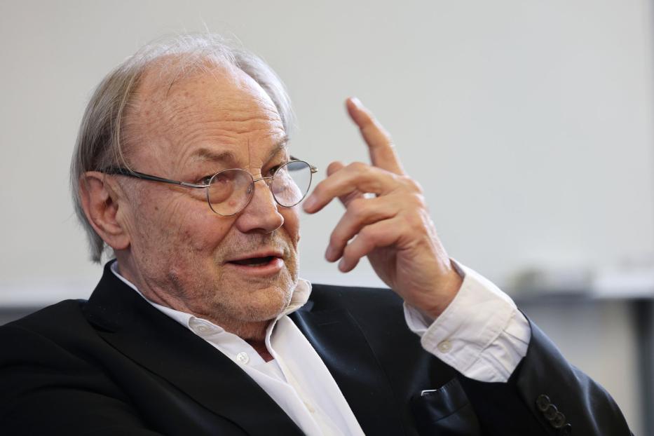 Ein älterer Mann mit Brille gestikuliert mit erhobenem Zeigefinger.