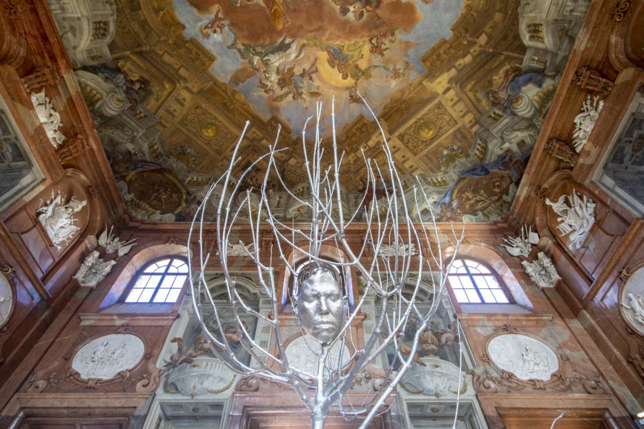 Eine silberne Skulptur eines Kopfes in einem Raum mit einem kunstvollen Deckengemälde.