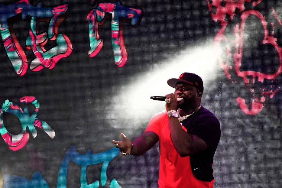 50 Cent tritt vor einer Leinwand mit dem Schriftzug „Get It Or“ auf.