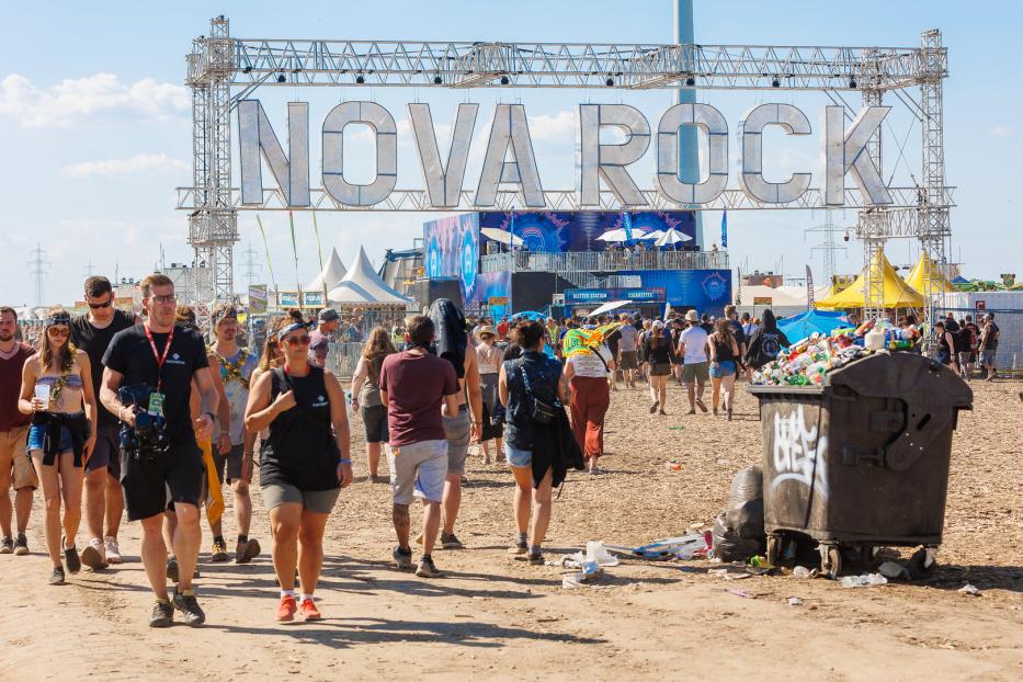Besucher strömen zum Nova Rock Festival unter einem großen „Nova Rock“-Schild hindurch.