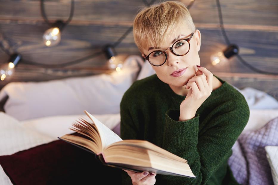 Eine Frau mit Brille liest ein Buch im Bett.