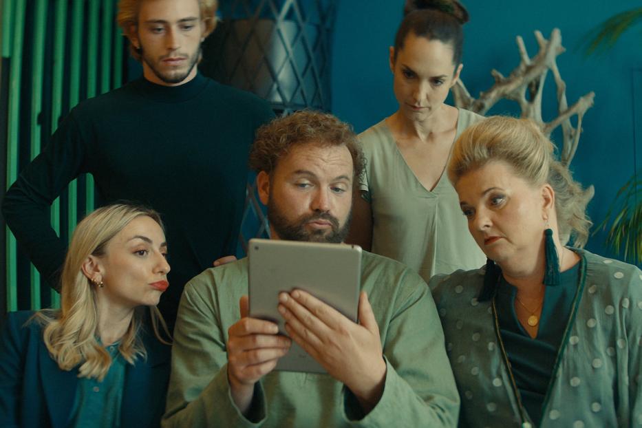 Eine Gruppe von fünf Personen schaut aufmerksam auf ein Tablet in einem Wohnzimmer.