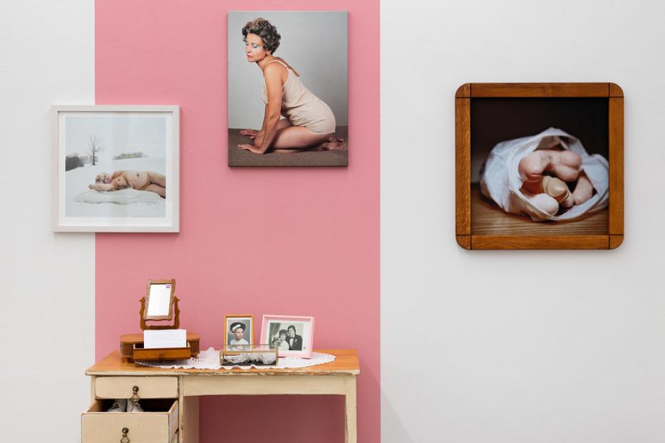 Eine Kunstinstallation mit Fotografien, einem Schminktisch und einem Korb mit Haarteilen.